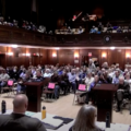 2024 Town Meeting in Arlington. The main floor of Town Hall is crowded, and the second floor balcony is also largely full of people.